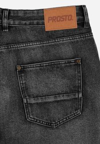 Czarne dżinsy z denimu mają skórzaną metkę z napisem "PROSTO" w pasie, tylną kieszeń z detalem w postaci przeszyć oraz metalowe elementy.