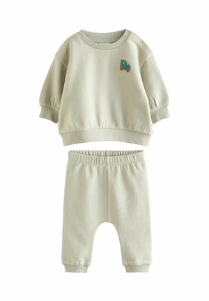 Weiches beiges Baby-Outfit mit langärmligem Oberteil, das einen kleinen blauen und orangefarbenen Traktor-Patch zeigt, kombiniert mit Hosen mit elastischem Bund.