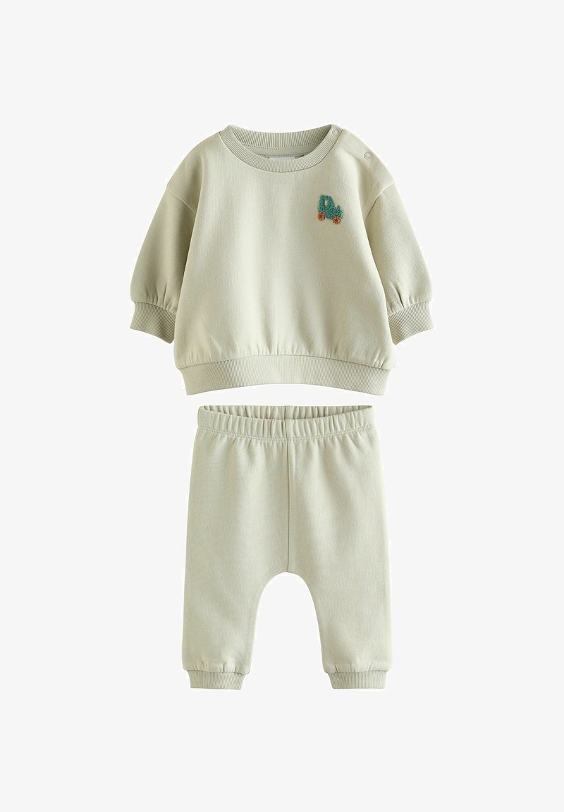 Ensemble bébé beige doux avec un haut à manches longues orné d'un petit patch de tracteur bleu et orange, associé à un pantalon à taille élastique.