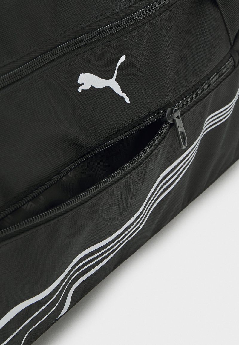 Sac de sport en tissu noir avec un logo blanc de Puma et trois bandes courbes blanches courant le long du côté, accompagné d'une poche avant zippée.