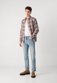 Plaid shirt in blue, red, and yellow, worn open over a white tank top; light blue jeans with slight distressing; brown loafers.