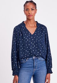Marinebluse mit silbernem Blumenmuster, V-Ausschnitt und gerafften Bündchen. Hergestellt aus leichtem Stoff, hat lange Ärmel und einen lässigen Schnitt.