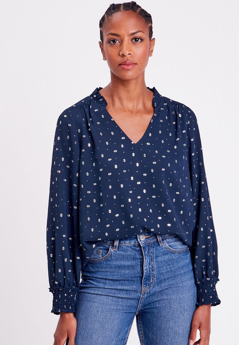 Marinebluse mit silbernem Blumenmuster, V-Ausschnitt und gerafften Bündchen. Hergestellt aus leichtem Stoff, hat lange Ärmel und einen lässigen Schnitt.