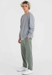 Lichtgrijze sweatshirt met lange mouwen en geribbelde cuffs. Olijfgroene broeken met zakken. Witte sneakers met perforatiedetails en logo.
