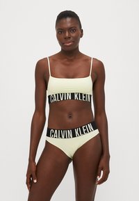Lichtgroene bikini-set met een crop top met dunne bandjes en een zwarte logo-tailleband. Gladde textuur met een minimalistisch ontwerp.