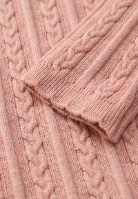 Weiches pinkes Strickgewebe mit einem strukturierten Kabelmuster und gerippten Akzenten, das ein gemütliches Gefühl vermittelt und am Saum leicht ausgefranst ist.