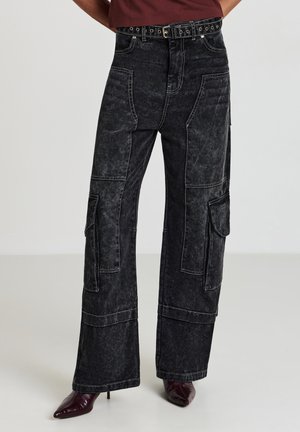 Schwarz hoch taillierte Cargo-Jeans mit verblasster Waschung, mehreren Taschen und kontrastierenden Nähten. Abgeschlossen mit einem Gürtel mit Metallnieten.