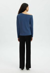 Blaues langärmliges Hemd mit Off-Shoulder-Design, kombiniert mit schwarzen weitem Hosen, die eine glatte Textur und minimalistische Details aufweisen.
