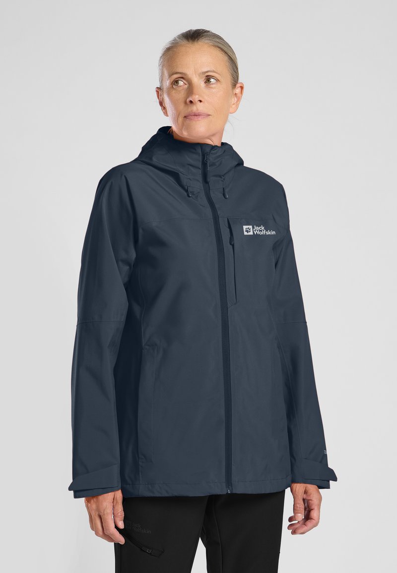 Veste imperméable navy avec capuche, fermeture éclair intégrale, logo sur la poitrine et poignets élastiques. Texture lisse, design décontracté, adaptée à un usage en extérieur.