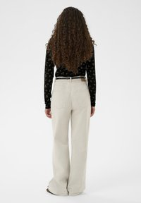 Svetlo béžové široké nohavice s vysokým pásom, zadnými vreckami a čiernym opaskom. Textúra látky je jemná a hladká.