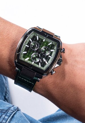 Green dial wristwatch with a square case, silver accents, and black chronograph sub-dials. Features a green leather strap with a textured surface.