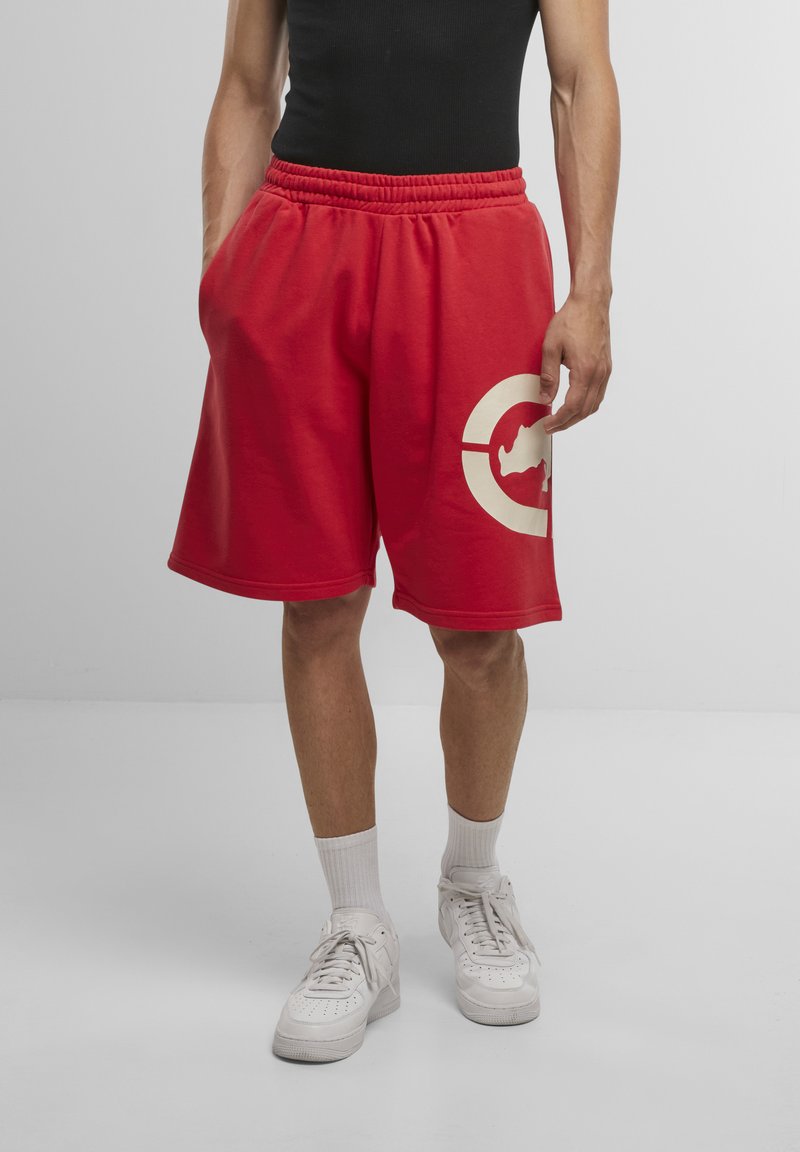 Shorts en coton rouges avec une taille élastique, des poches latérales et un grand logo circulaire crème comportant une silhouette.