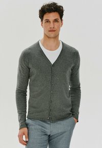 Ciemnoszary kardigan z dekoltem w serek, pięcioma guzikami z przodu i długimi rękawami, w zestawie z białym t-shirtem i jasnoniebieskimi spodniami.