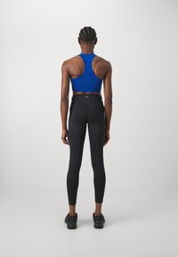 Blå sportbehå med racerback-design som matchas med svarta högmidjade leggings. Båda plaggen är åtsittande och har en struktur med en slät yta.