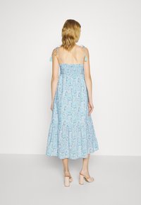 Ljusblommig sommarklänning med justerbara axelband, smockad midja, utsvängd kjol och näsdukdetaljer. Bärs med beige blockklack-sandaler.