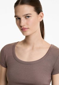 Top corto a maniche corte marrone a costine con scollatura ampia a barca. Texture morbida e design aderente, che mette in risalto il contorno del capo.