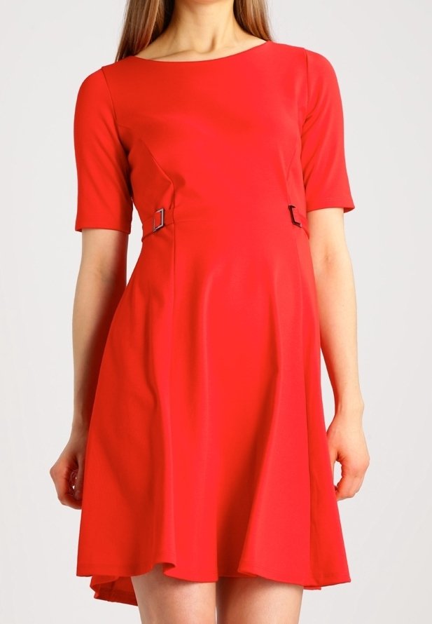 Femme portant une robe rouge vif longueur genou avec des manches courtes et de petits détails de boucle à la taille.