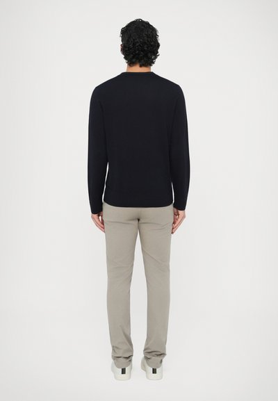 Granatowy sweter z okrągłym dekoltem i prążkowanym dołem, zestawiony z jasnobeżowymi spodniami. Model nosi białe buty z wielokolorowymi paskami na pięcie.