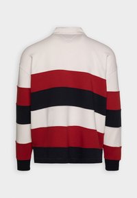 Pullover a righe in rosso, nero, bianco e blu. Caratterizzato da un colletto, maniche lunghe e polsini a coste realizzati in un morbido tessuto testurizzato.