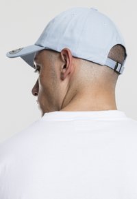 Cappellino azzurro chiaro in cotone con visiera curva, cinturino regolabile sul retro e logo circolare sul lato sinistro.