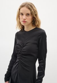 Must mustriidzad dress, millel on pikad varrukad ja sujuv kangas, esiosas on kogumised ning mansetid on kitsendatud, et saavutada vormikas sobivus.