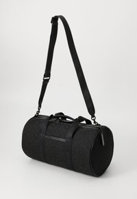 Schwarze Reisetasche in runder Form, aus Stoffmaterial mit geprägtem Muster, mit zwei Griffen und einem verstellbaren Schultergurt.
