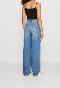 Szerokie dżinsy w kolorze niebieskim wykonane z denimu, z wysokim stanem, pięcioma kieszeniami i lekko wyblakłym efektem, zestawione z czarnym topem na ramiączkach.
