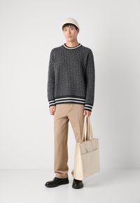 Svart-hvitt mønstrete genser med rund hals, beige bukser, svarte sko og en kremfarget totebag med frontlomme.