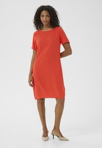Robe à manches courtes en tissu orange vif, dotée d'une coupe ample, d'un col rond et de deux poches latérales. Portée avec des chaussures à talons beiges.