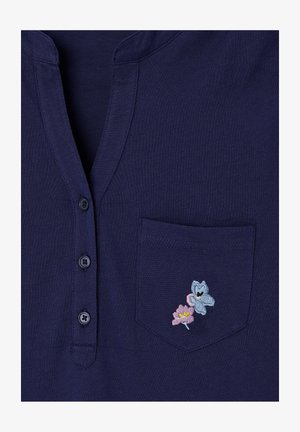 Chemise bleu foncé avec trois boutons et une poche poitrine ornée de petites fleurs brodées roses et bleues.