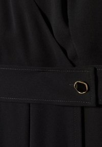 Tissu noir avec une large ceinture à petite boucle dorée irrégulière avec un détail noir au centre.