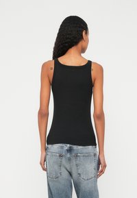 Μαύρο εφαρμοστό τοπ χωρίς μανίκια με στρογγυλή λαιμόκοψη και φαρδιές τιράντες, κατασκευασμένο από λείο ύφασμα· φορεμένο με ανοιχτόχρωμα τζιν παντελόνια.