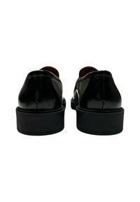 Scarpe in vernice nera con finitura liscia, suola piatta bassa e tacco arrotondato. Presentano dettagli a pannello in contrasto sui lati.