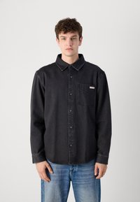 Black denim shirt with a button-up design, long sleeves, collar, and chest pocket. Features a small brand label on the pocket.