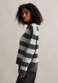 Pull rayé gris et gris clair avec un col montant et des poignets côtelés. Texture en laine douce, coupe décontractée et vue de profil latéral.