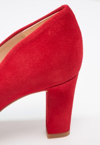 Escarpin rouge en suede avec un large talon, présentant une finition lisse et mate ainsi qu'un design à bout pointu.