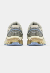 Beige sportcipők, légáteresztő hálós felsőrésszel, szürke akcentusokkal és gél párnázási rendszerrel. Világoskék és barna színű texturált talppal rendelkezik.