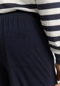 Krupan pogled na osobu koja nosi tamnoplave hlače s stražnjim džepom i bijelu košulju s tamnoplavim horizontalnim prugama na rukavu.