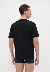 T-shirt nero a maniche corte in cotone, con un design a collo rotondo. Texture liscia senza motivi o accenti visibili.