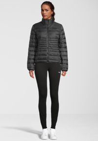 Giubbotto imbottito nero con cuciture orizzontali, colletto alto e chiusura con zip. Abbinato a leggins neri e sneaker bianche.