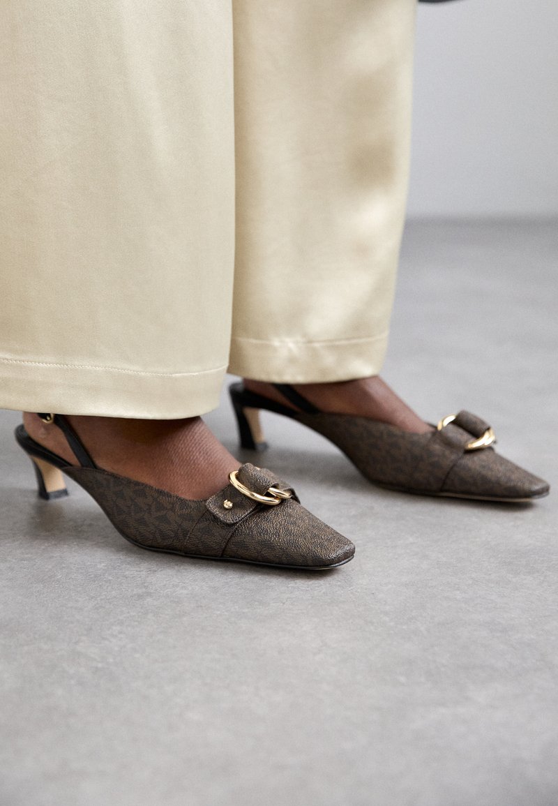 Talons slingbacks marron à motifs avec un bout pointu, accent en métal doré et un talon fin, associés à un pantalon large de couleur crème.