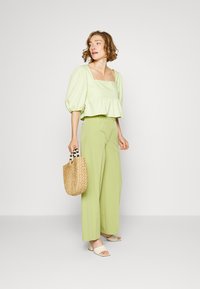 Top verde claro com mangas bufantes e decote quadrado, combinado com calças largas na mesma tonalidade. Bolsa de palha e sapatos de salto quadrado e aberto na frente.