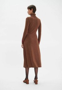 Robe en tricot marron avec un col haut, des manches longues et une longueur mi-mollet. Présente des poignets violets et une taille cintrée. Texture lisse.