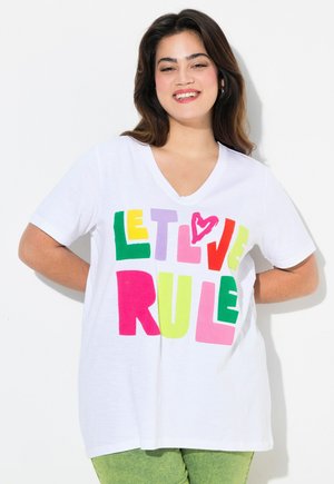 T-shirt blanc avec un col en V, arborant des lettres en blocs audacieuses et multicolores écrivant "LAISSE L'AMOUR RÉGNER" en vert, jaune, rose, violet et rouge.