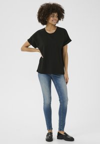 Juoda trumpa rankovė viršutinė dalis su apvalia apykakle, derinama su priglundantčiomis mėlynomis džinsinėmis kelnėmis ir juodais loaferiais, pasižyminti lygiu tekstūru ir kasdiene dizaino estetika.