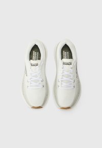 Zapatillas deportivas blancas con parte superior de malla, cierre de cordones y ligera amortiguación. Presenta un acento dorado texturizado en la suela y detalles de marca.