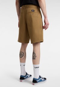 Hnědé bavlněné kraťasy s zadní kapsou, doplněné modrými teniskami a bílými ponožkami s logem Vans. Jednoduchý, rovný střih.