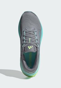 Scarpa da ginnastica grigia con tomaia in mesh testurizzato, dettagli turchesi, particolari riflettenti e logo verde sulla linguetta.