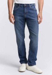 Jeans in denim blu con vestibilità dritta, dotati di cinque tasche, cuciture discrete e chiusura con bottone, abbinati a sneakers bianche.