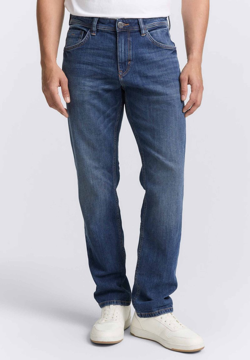 Jeans in denim blu con vestibilità dritta, dotati di cinque tasche, cuciture discrete e chiusura con bottone, abbinati a sneakers bianche.